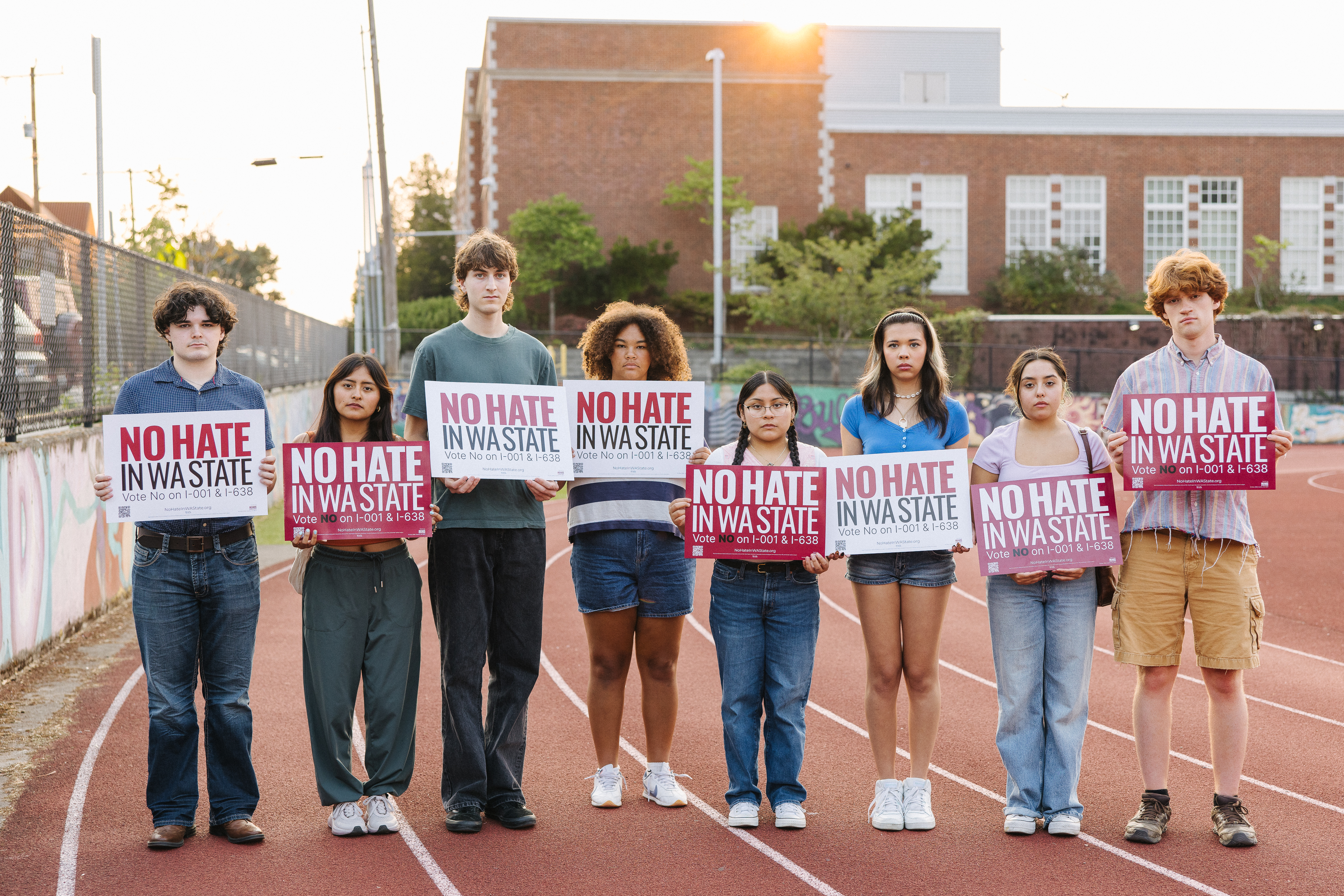 a group of kids holding "No Hate in WA State" signs on a track field