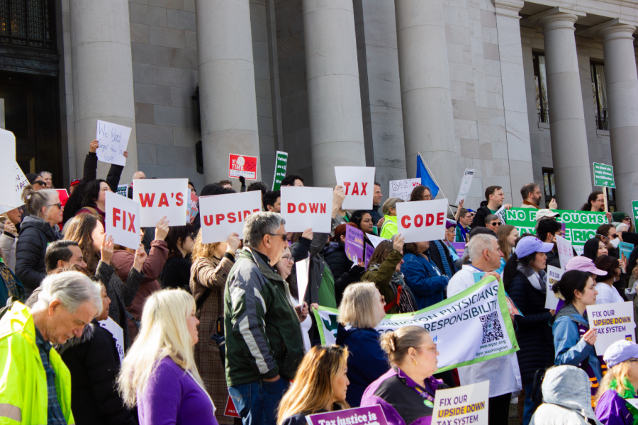 Fuse rally attendees hold signs saying "Fix WA's Upside down Tax Code" on the Capitol steps